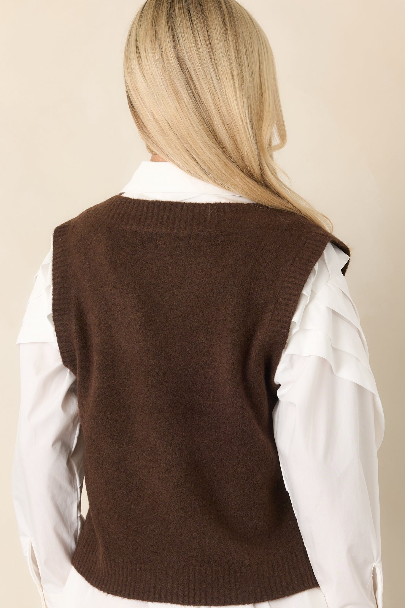 Rear view of the dark chocolate sleeveless vest, highlighting its clean layering silhouette, smooth back, and small side slits at the hem.