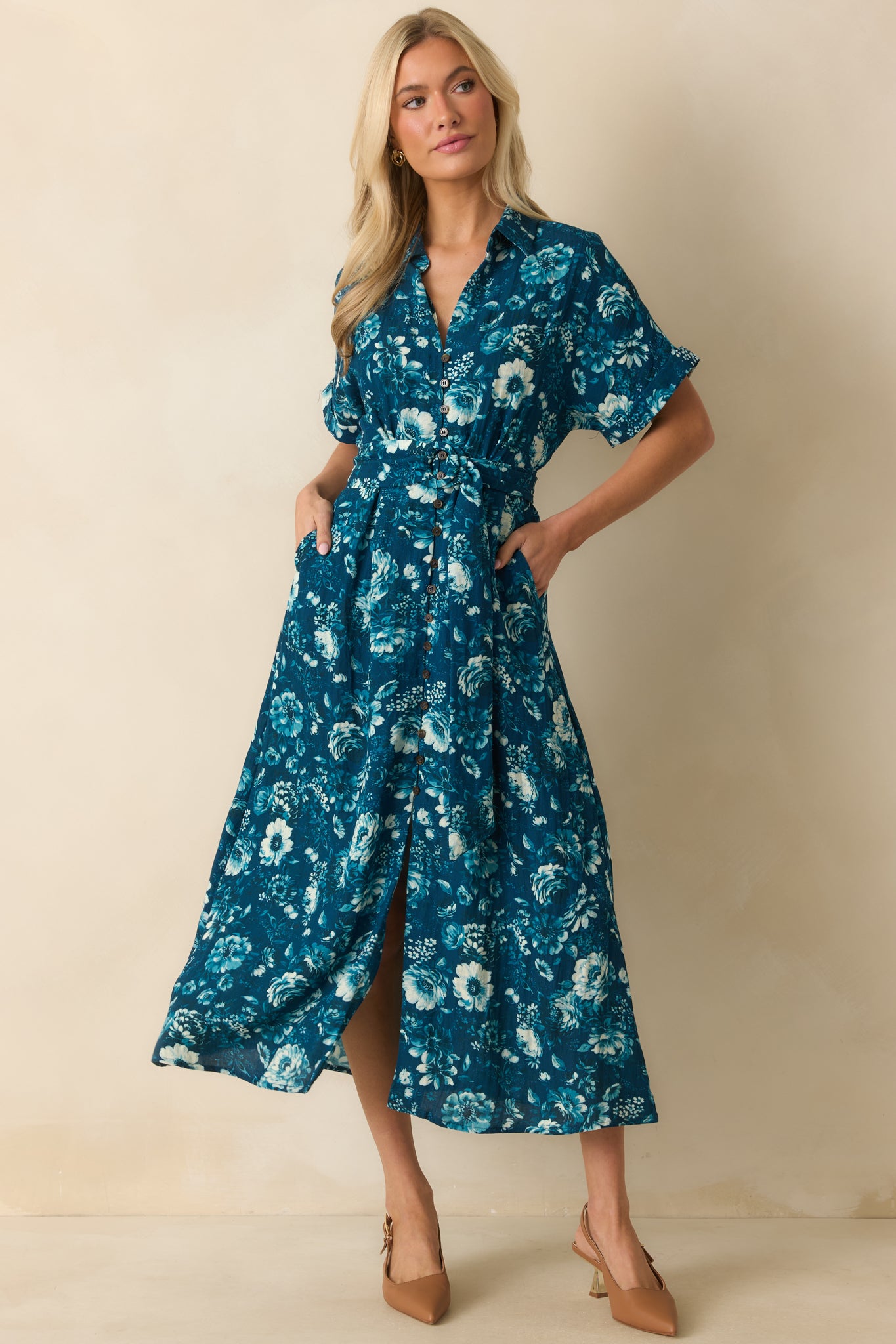 Dark teal dress with a blue multicolor floral print, collared v-neckline, and elastic waistband, featuring a pull-through belt and short cuffed sleeves.