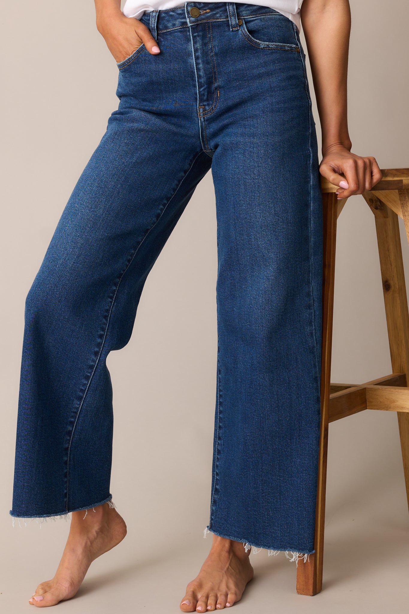 Dark wash wide-leg jeans with a slightly cropped length, raw bottom hem, functional pockets, and a classic button and zipper closure.