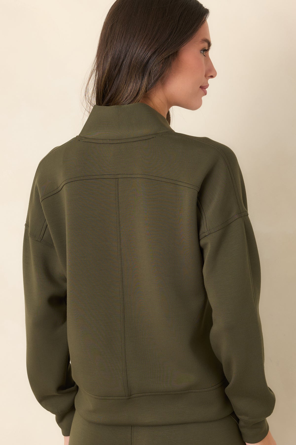 Rear of the deep olive-green top showing the relaxed silhouette, dropped shoulders, and long banded sleeves.