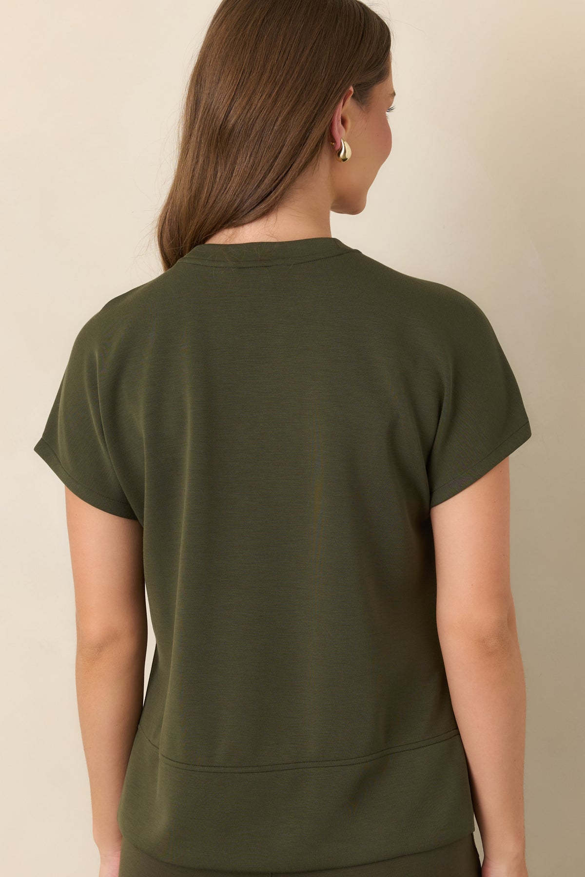 Rear view of the deep olive top showcasing its smooth fabric, short sleeves, elongated high-low hem, and side slits.