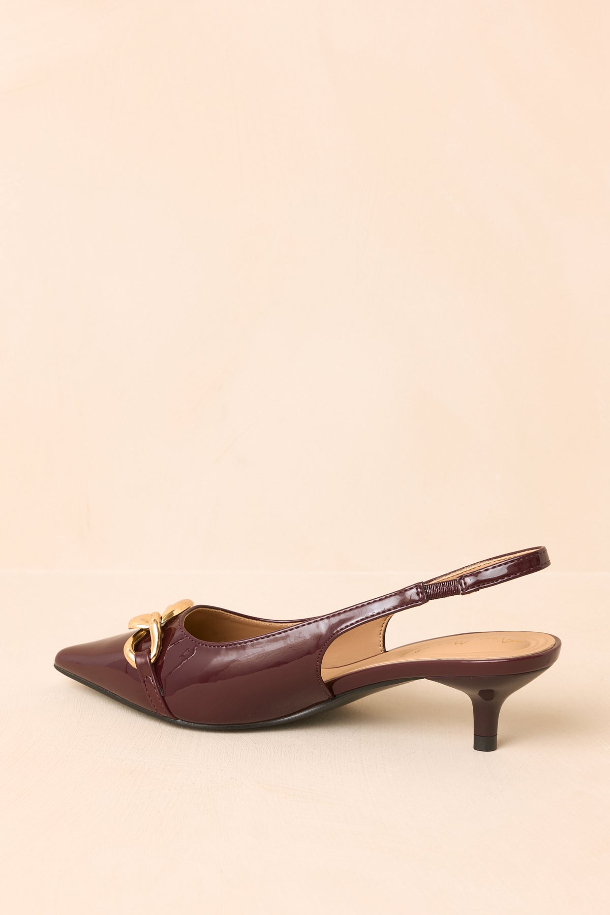 Rear of the deep plum patent slingback heels showing the open design, low kitten heels, and polished finish.