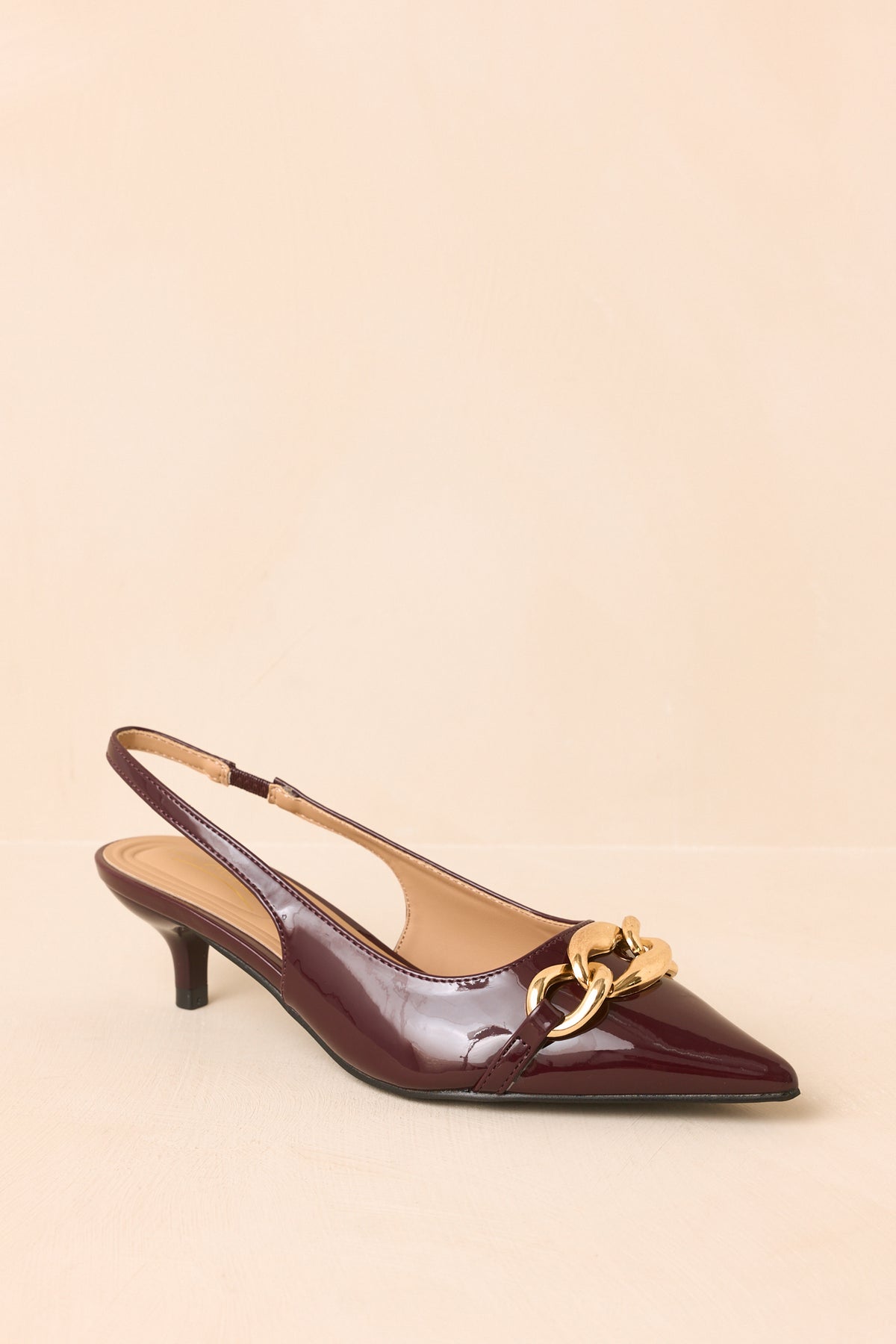 Deep plum patent slingback heels displaying their sharply pointed silhouette, oversized gold-tone chain, and low kitten heel.