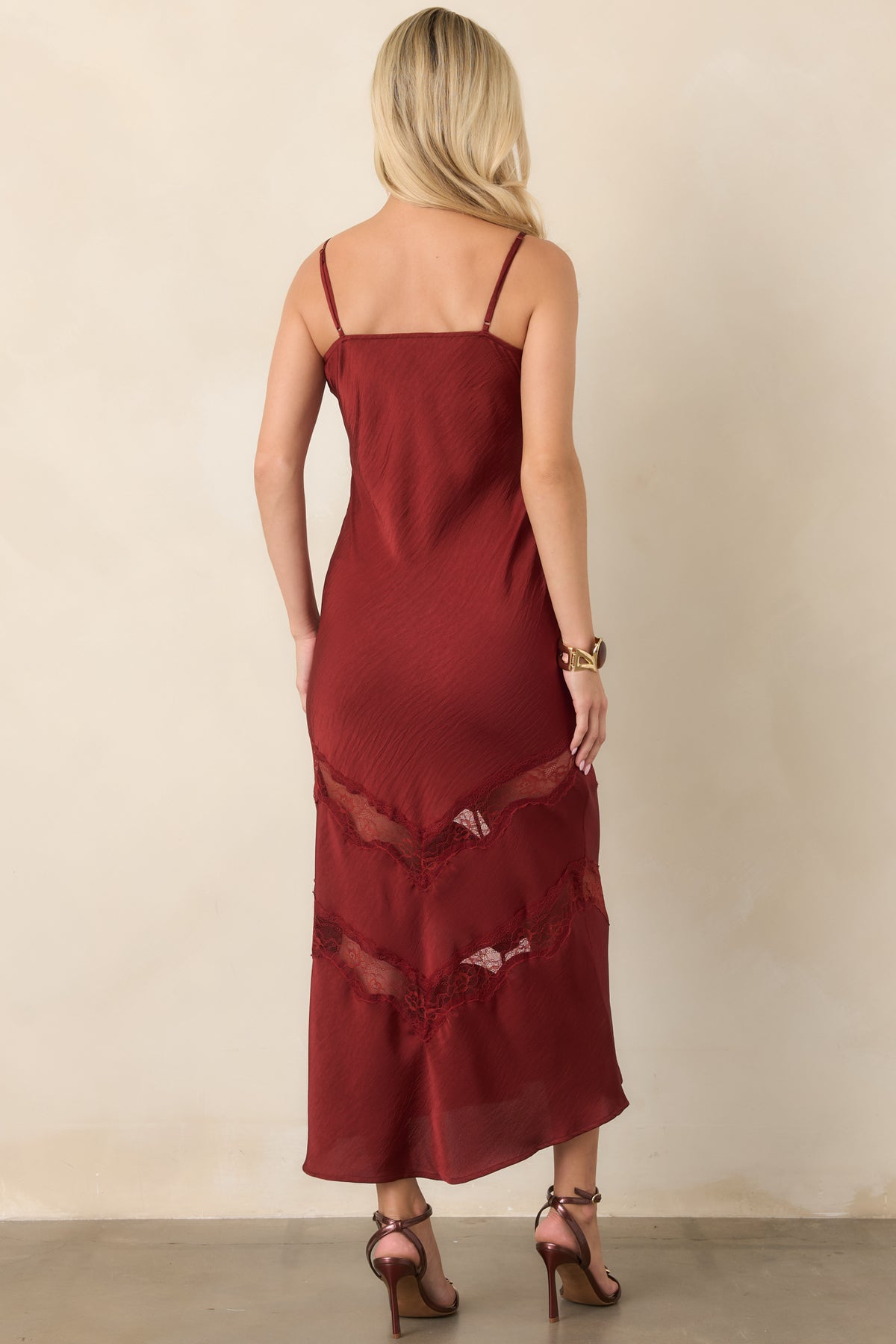 Back view of a deep red satin midi dress with slender adjustable straps and tonal lace detailing along the lower skirt