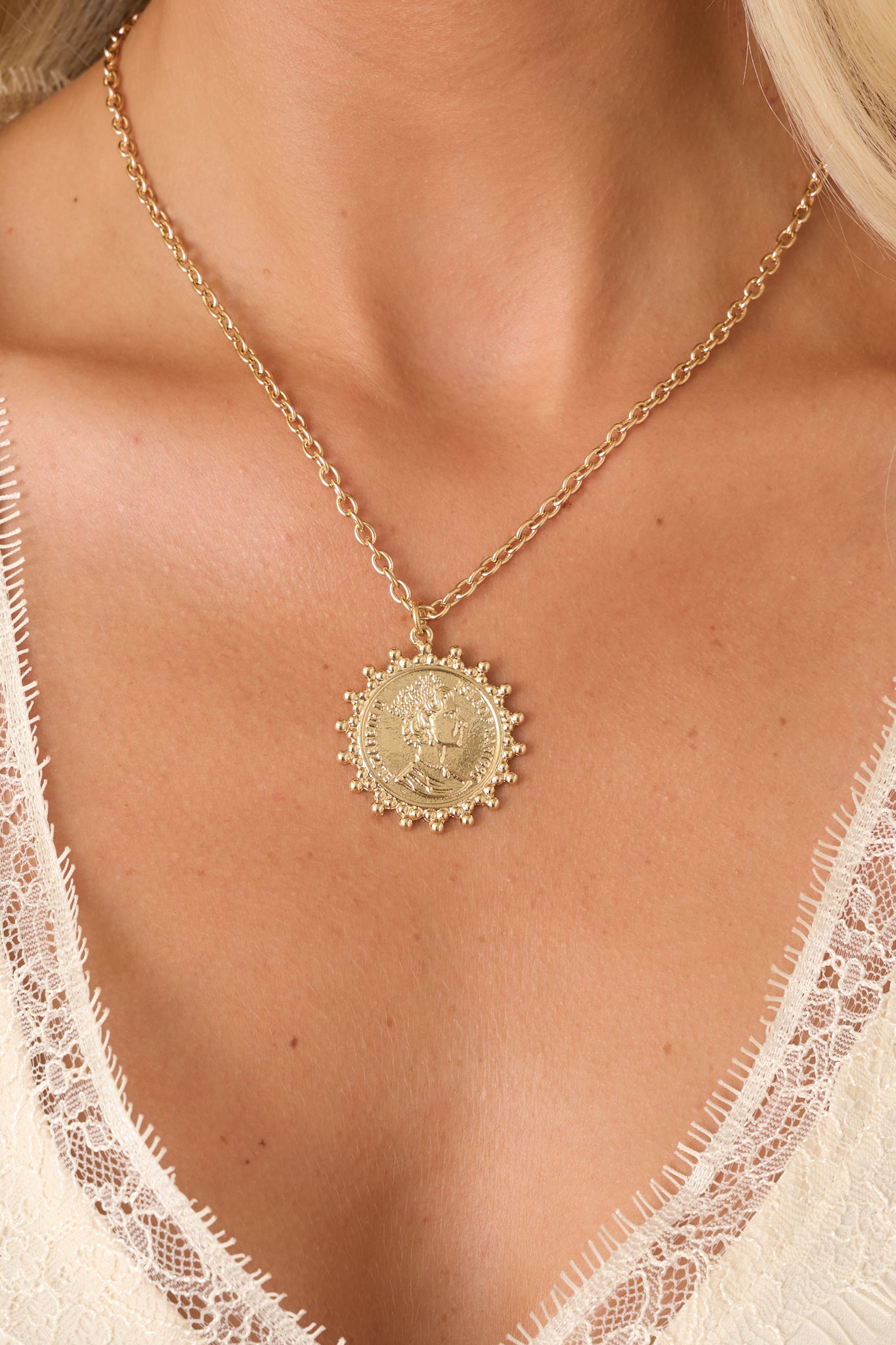 Delicate gold necklace showcasing a coin-style pendant with intricate detailing, textured beaded edging, and an adjustable extender chain.