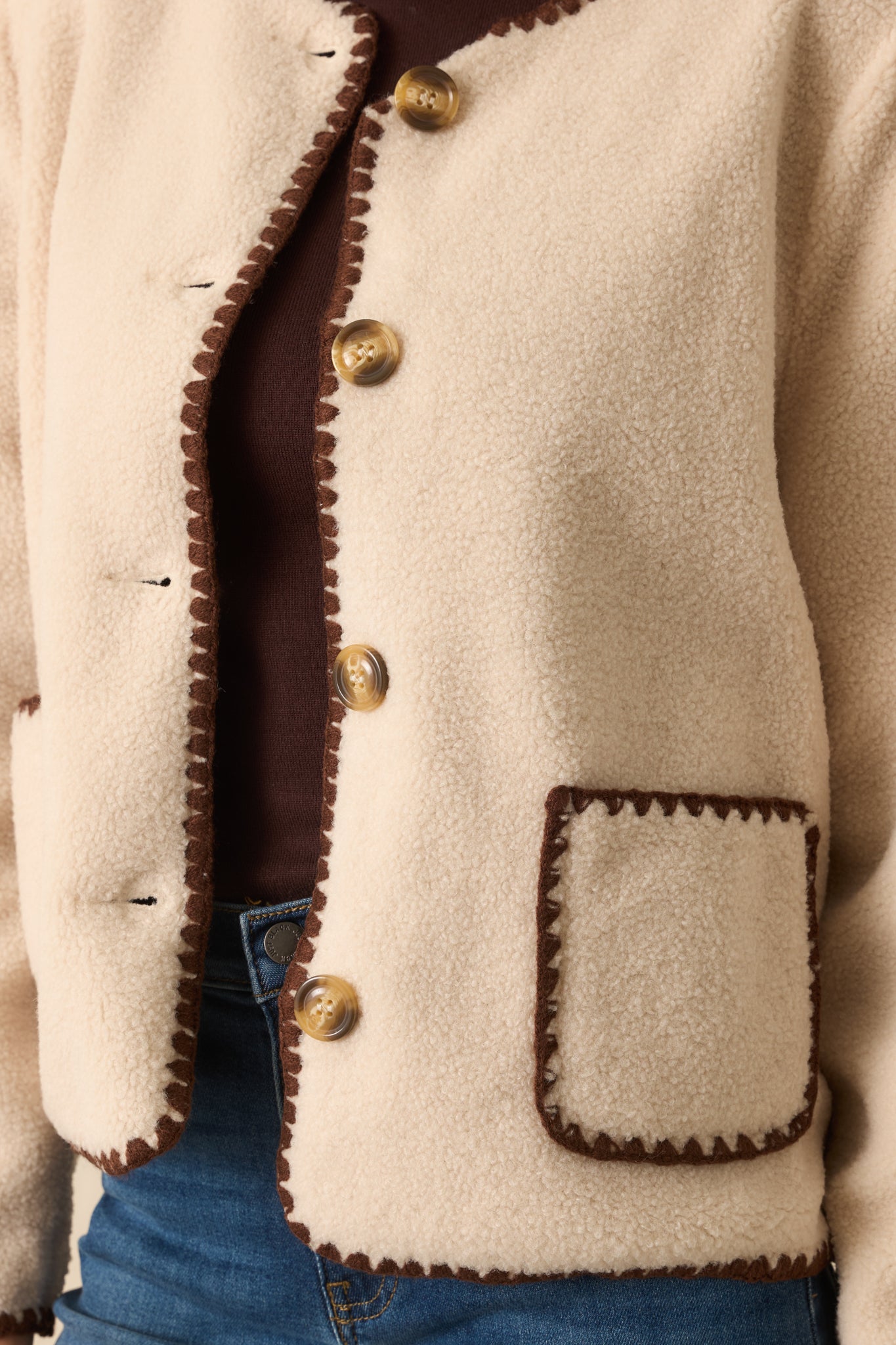 Tight detail of ivory sherpa fabric showing tortoise shell buttons and chocolate brown whipstitch accents.
