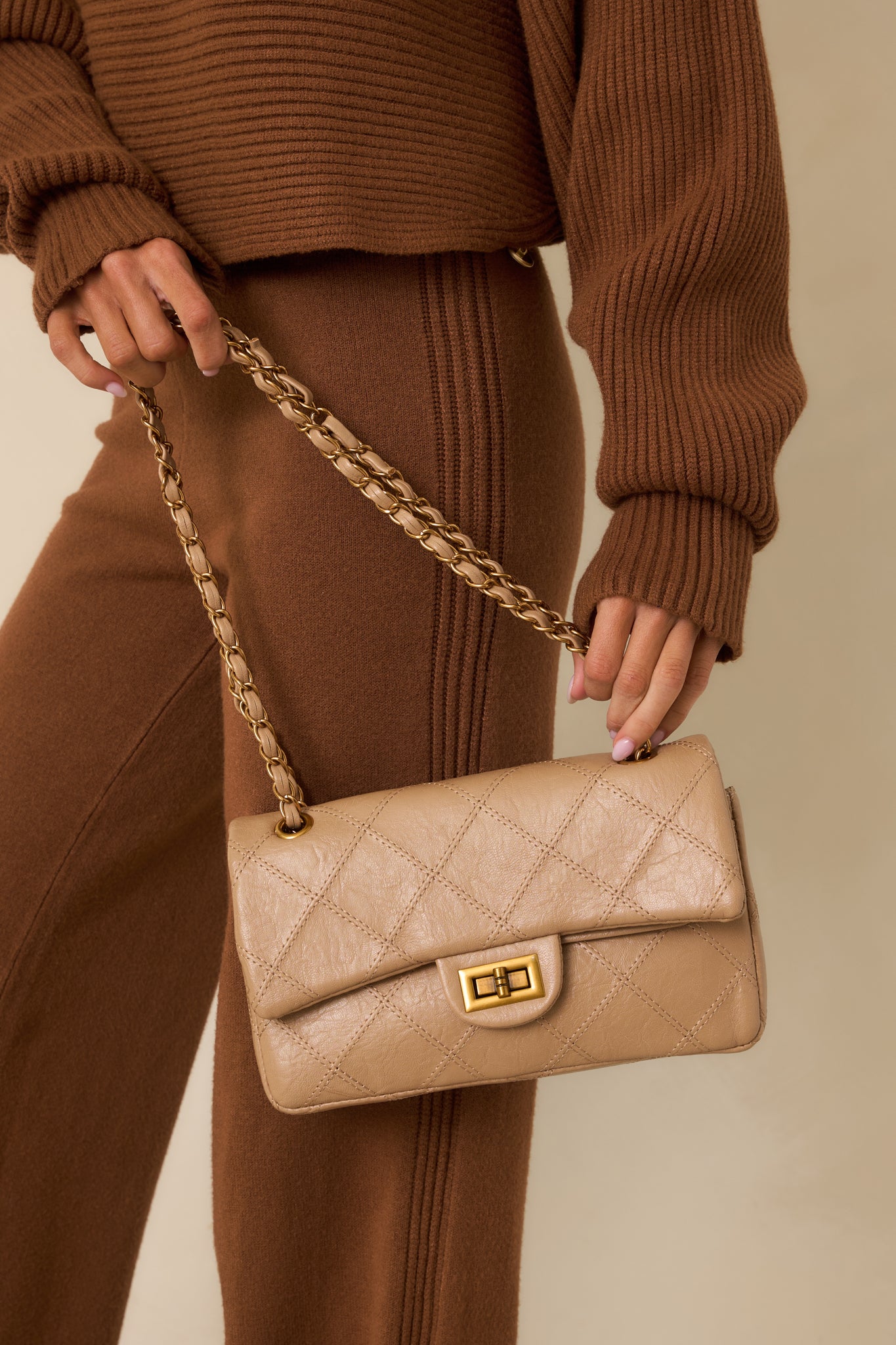 Close detail of the gold-tone turn-lock clasp centered on quilted beige faux leather.