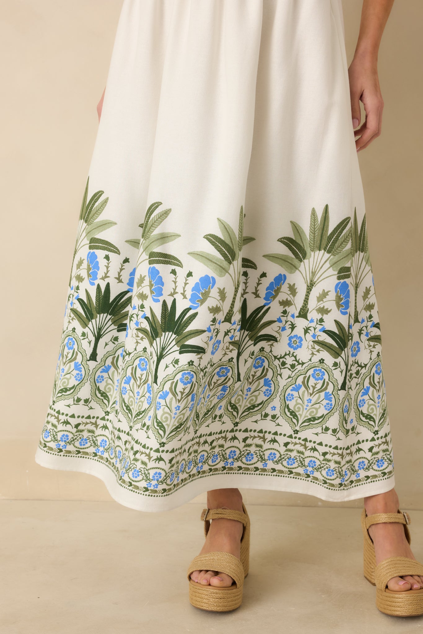 Detail of green and blue floral and palm border print along hem of ivory midi dress.