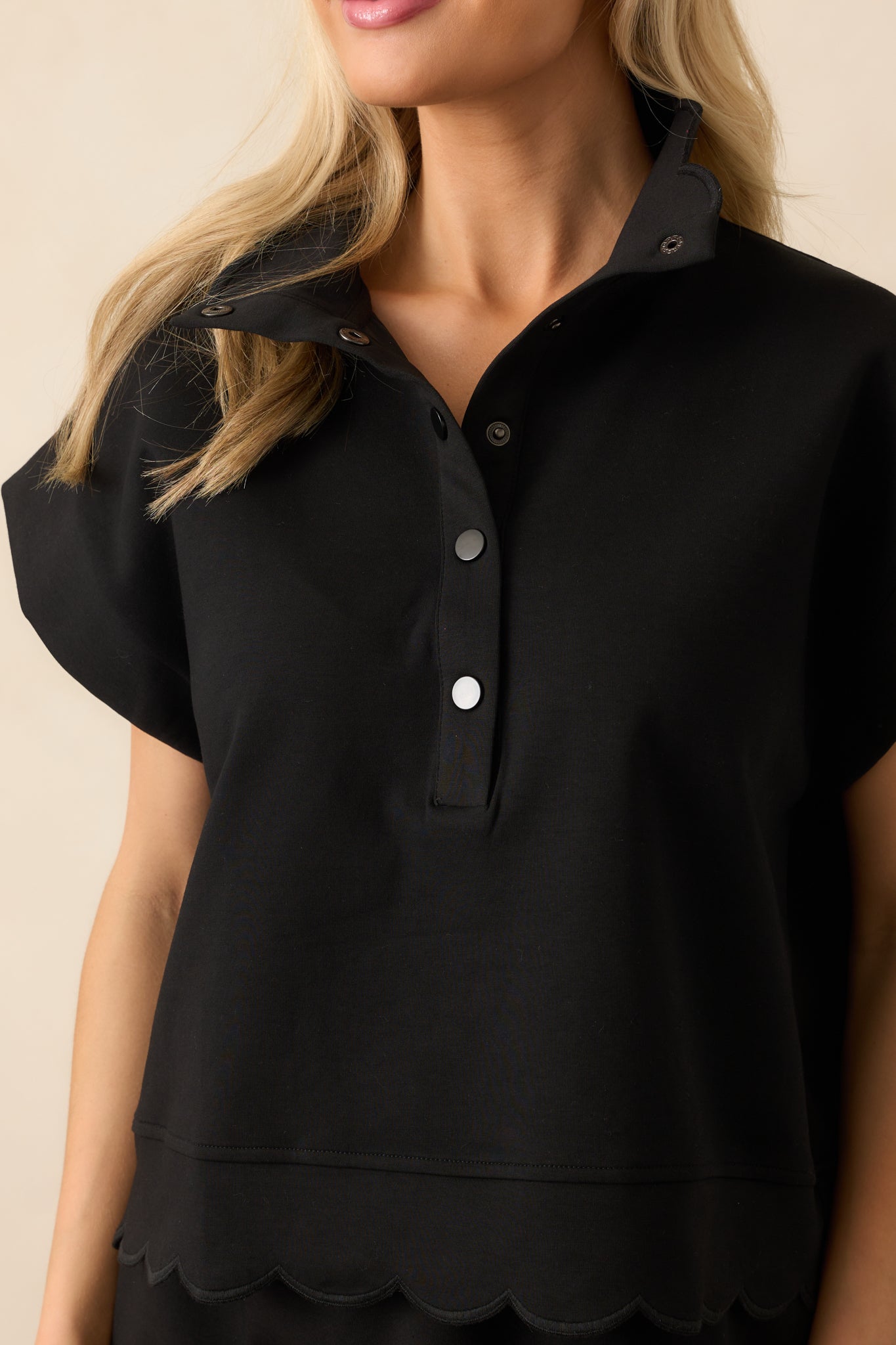 A detailed close-up of the scalloped hem embroidery and textured stitching along the sleeve and bottom edge.