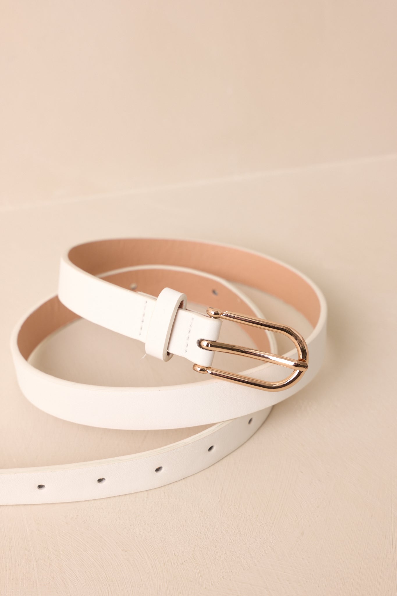 Close-up detail of the thin white faux leather belt showing the smooth texture and polished gold buckle.