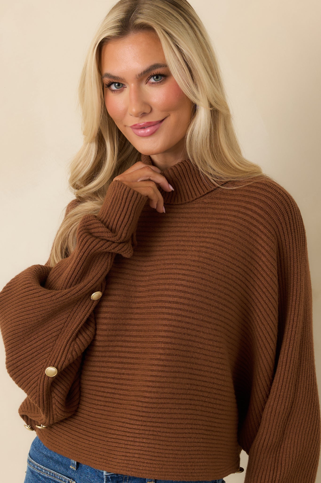 Detail of turtleneck and batwing sleeves on brown cropped sweater.
