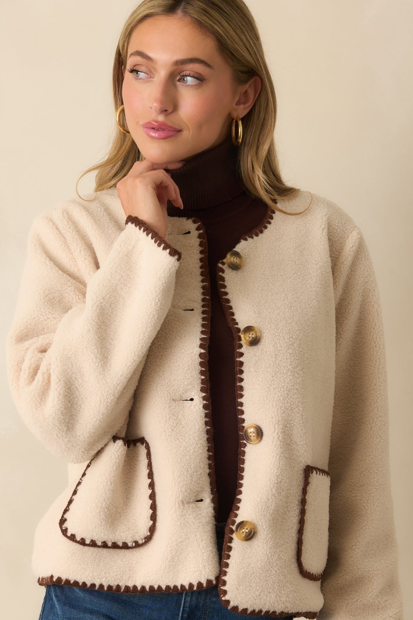 Detail of the patch pockets and whipstitch edges on the front of the ivory sherpa jacket.