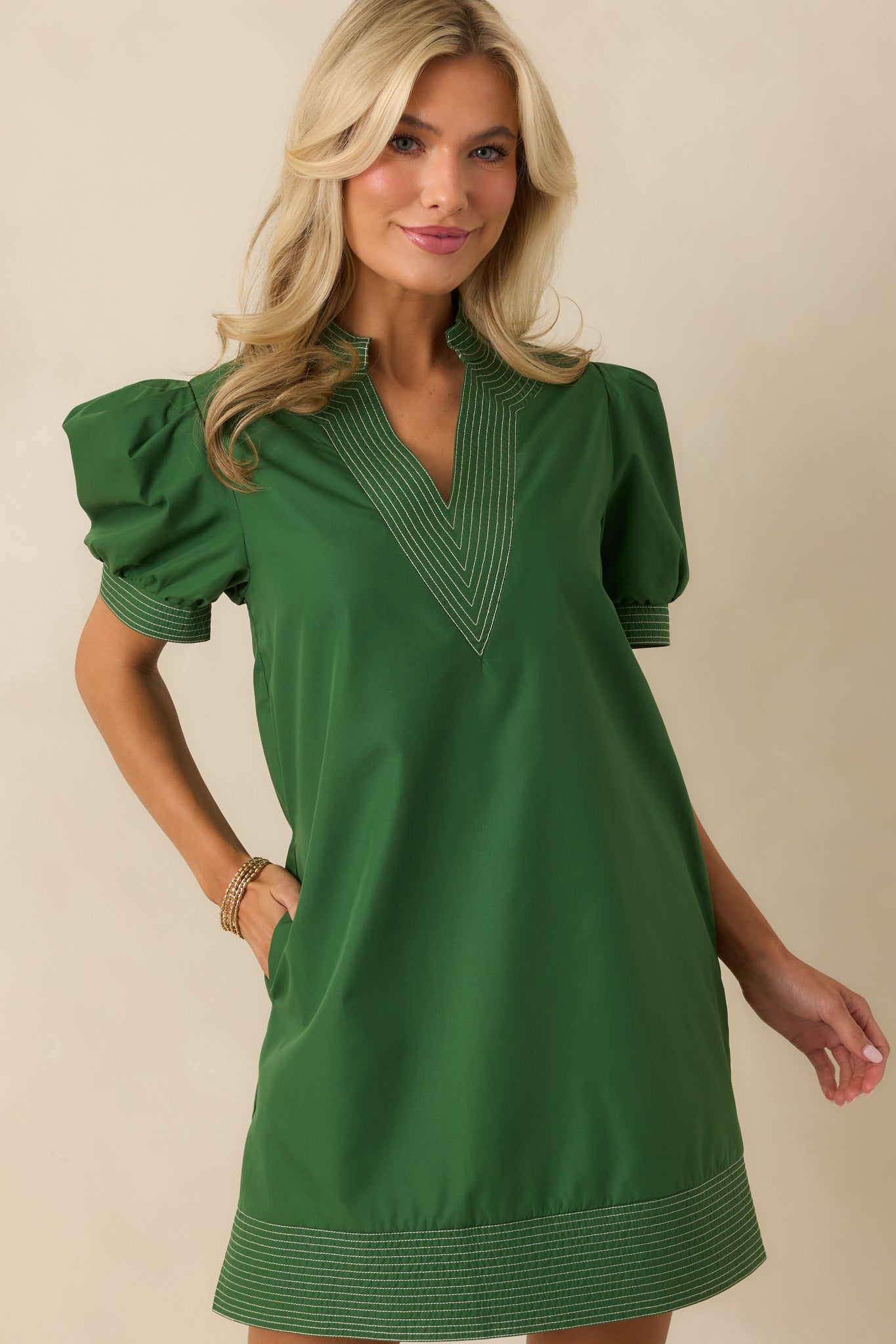 Detail of short puff sleeves and subtle white stitching on forest green mini dress.