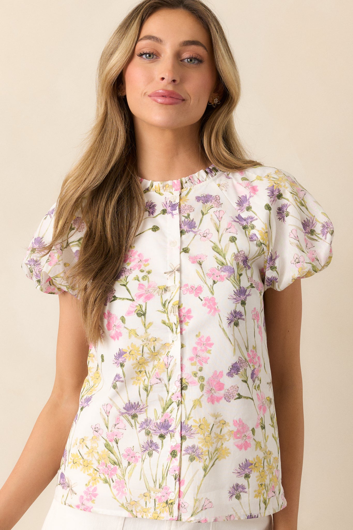 A detailed shot of the short puff sleeves with elastic cuffs and the ruffle trim neckline, showcasing the soft fabric and pink floral print on this ivory top.