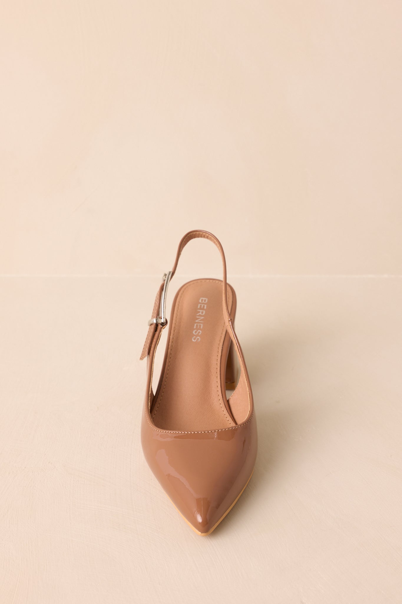 A straight-on detail of the camel brown heels showing the shiny patent finish and stitching around the pointed toe.