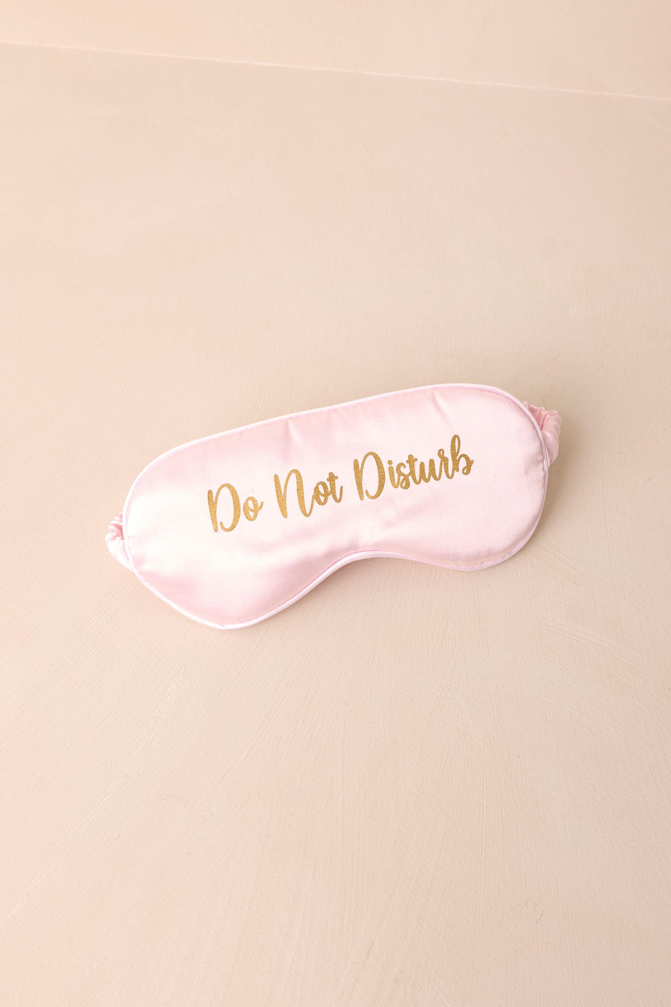 A detailed angle showcasing the gold lettering on the front, with "Do Not Disturb" elegantly displayed against the soft pink satin.