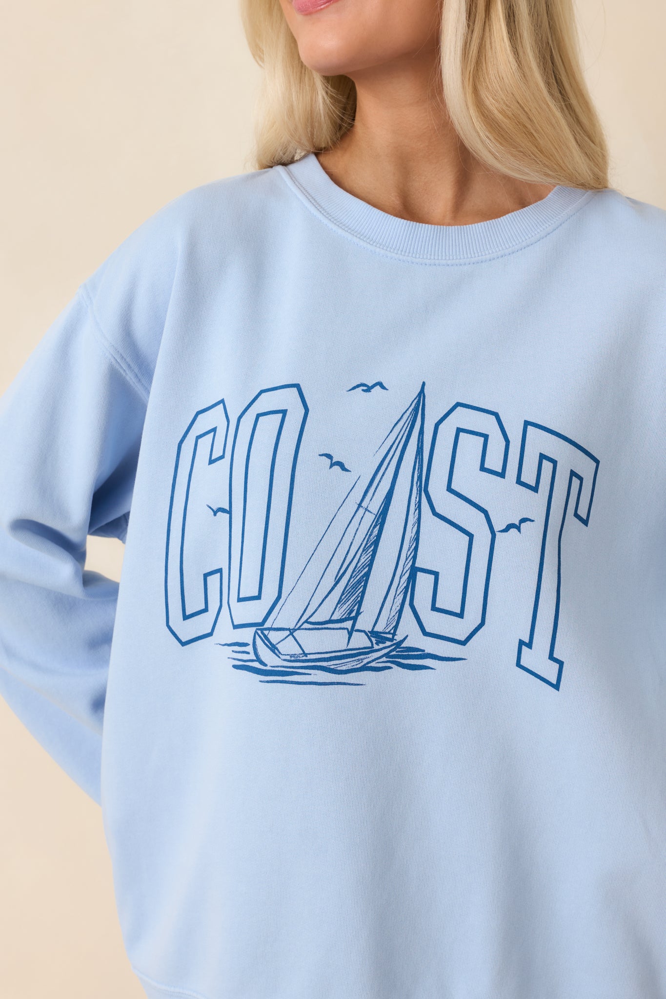 Detailed close-up of the “COAST” graphic, sailboat illustration, and ribbed hem on the sweatshirt.
