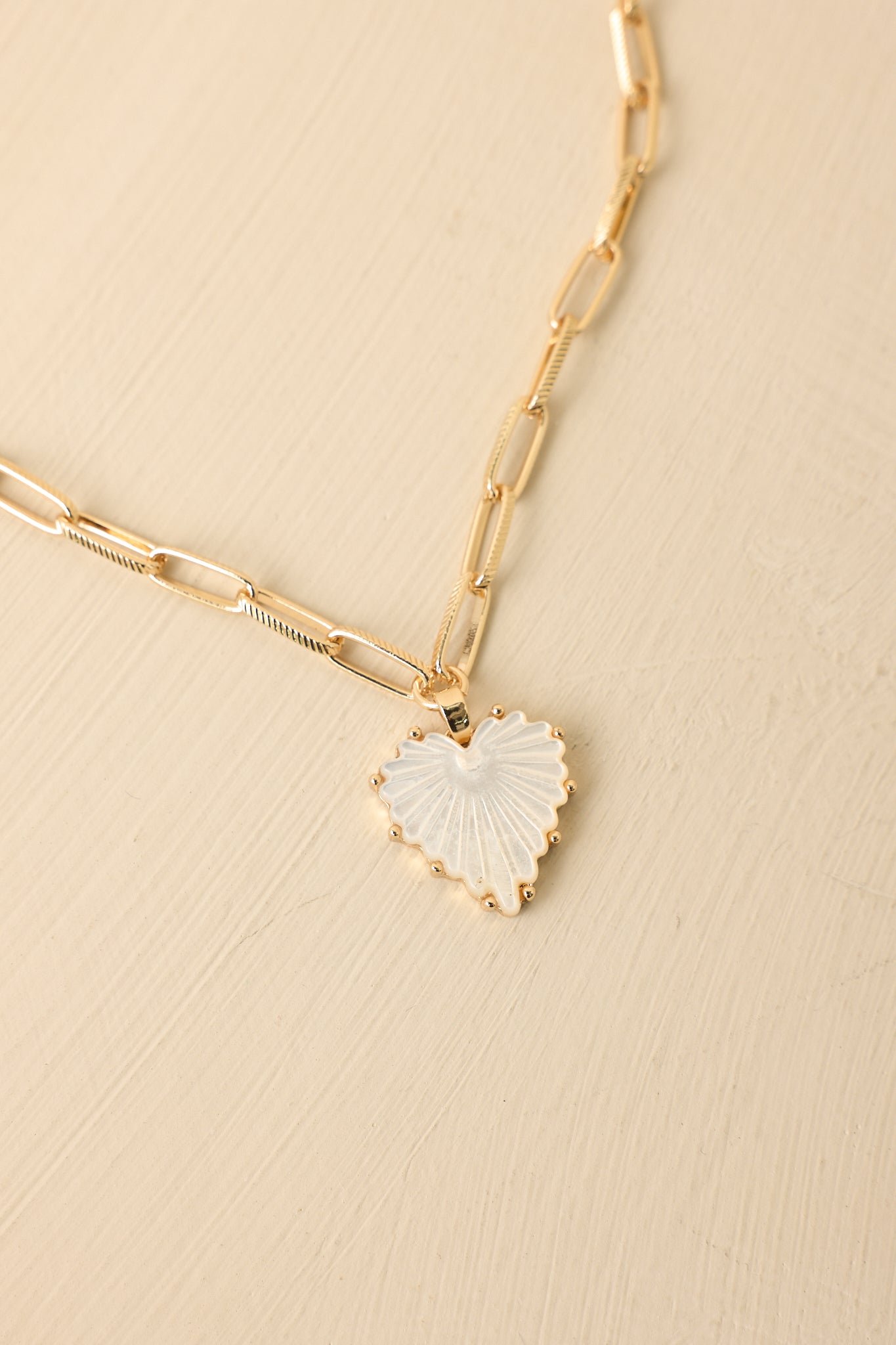 Detailed close-up of the scalloped heart pendant revealing its textured surface and the slim paperclip-style chain connection.
