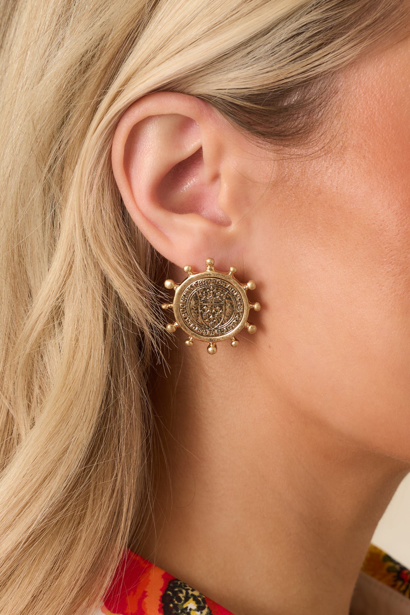 Detailed close-up of worn gold earrings showing embossed coin pattern and surrounding ball prong frame.