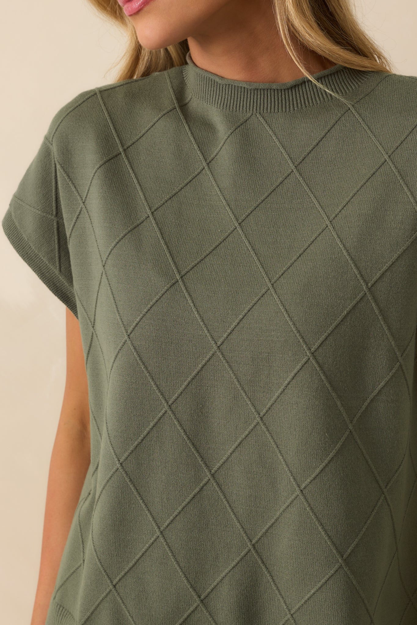 Detailed shot of green sweater showing argyle stitch pattern, rolled crew neckline, and folded sleeve cuffs.