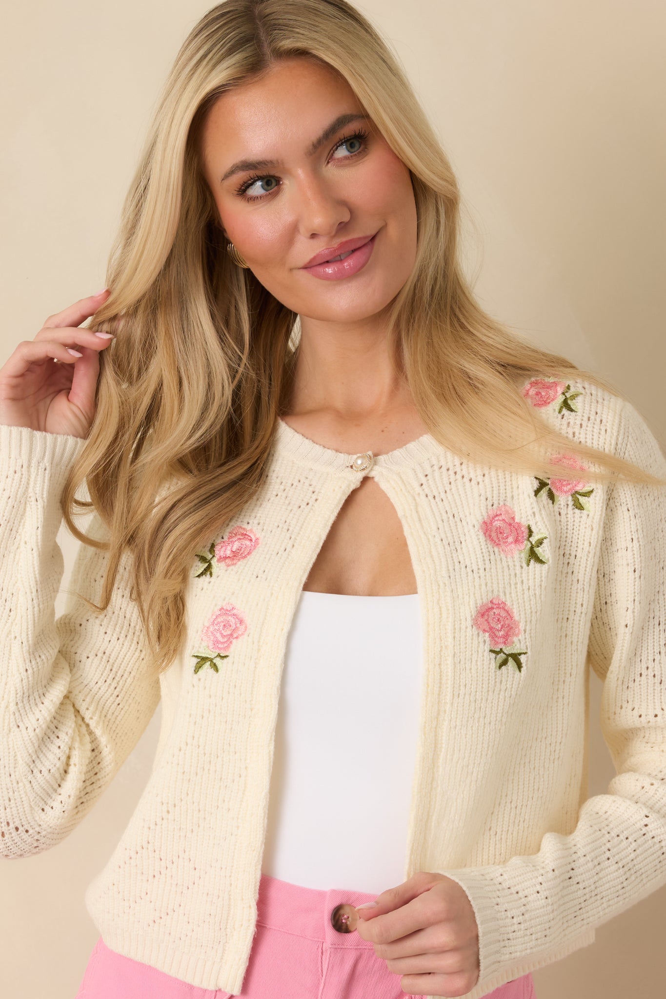 Detailed look at the lightweight ivory knit texture with pink bloom embroidery and a vintage-inspired pearl-style neckline closure.
