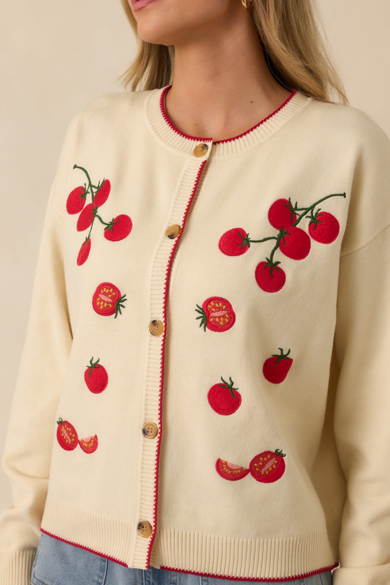 Detailed look at the ribbed trim, button-front closure, and cherry tomato embroidery on the ivory cardigan.