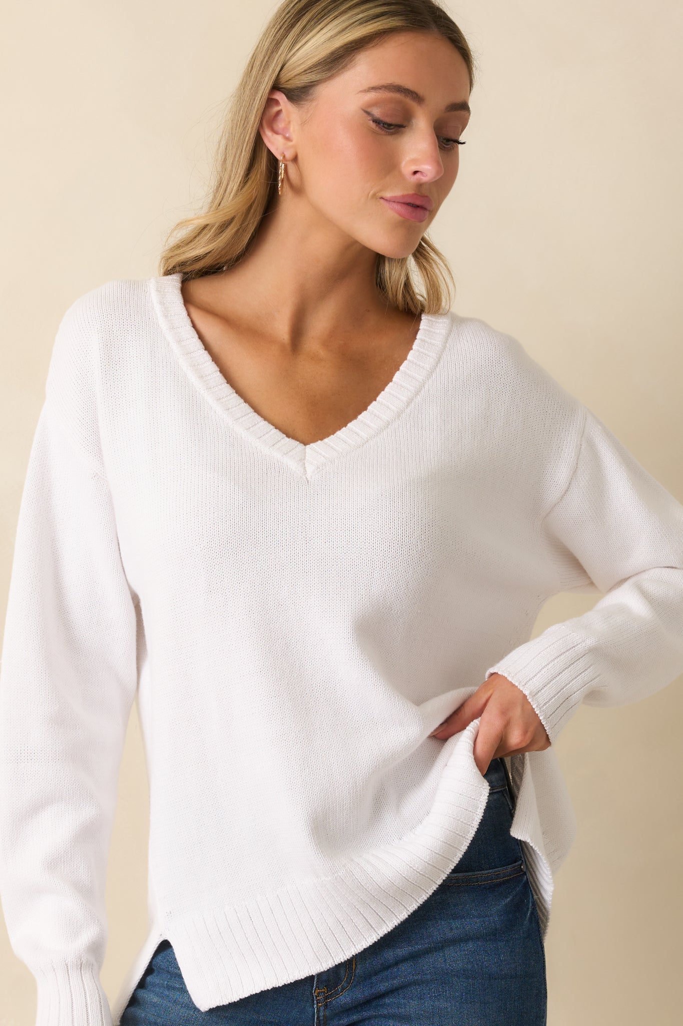 Detail of ribbed sleeve cuff and knit texture of relaxed-fit white sweater.