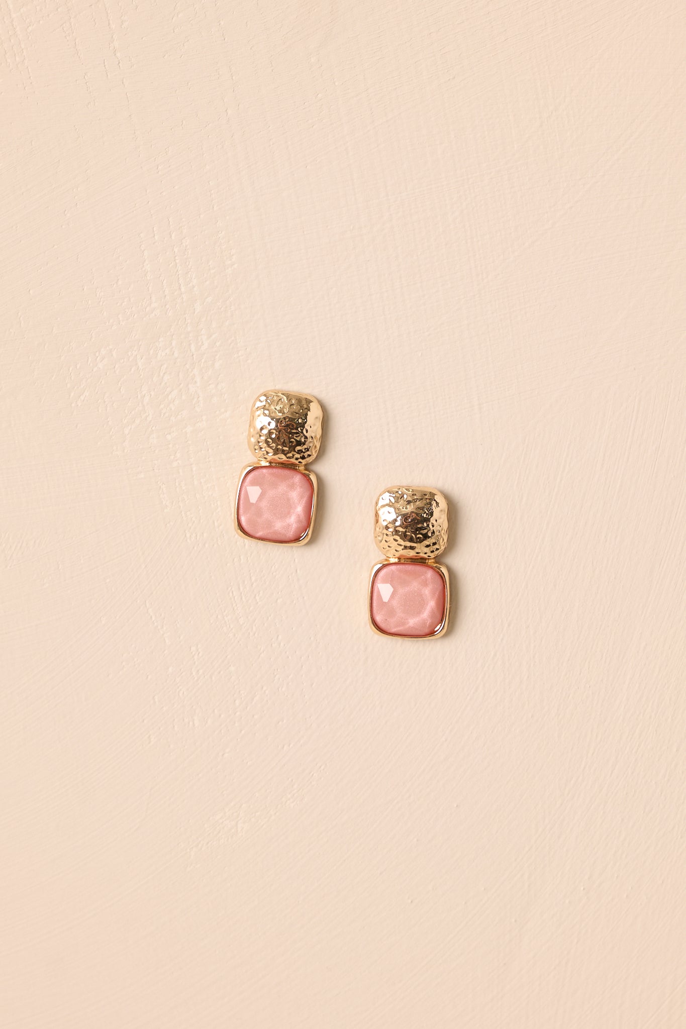 A detailed shot of the earrings highlighting the textured gold square studs and pink bezel-set gemstones.
