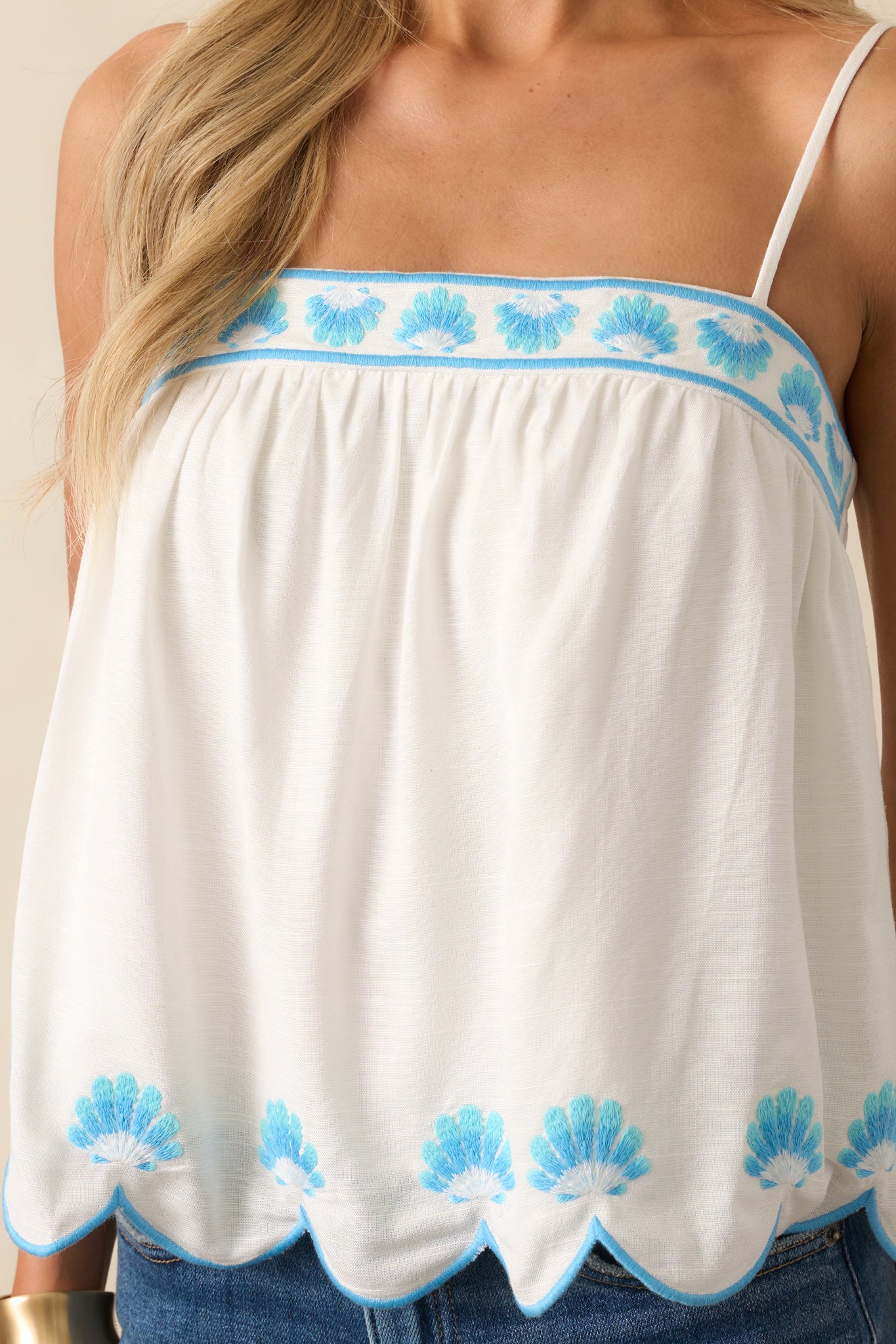 Detailed shot of the blue embroidered scallop shell motifs and textured stitching on the white fabric.