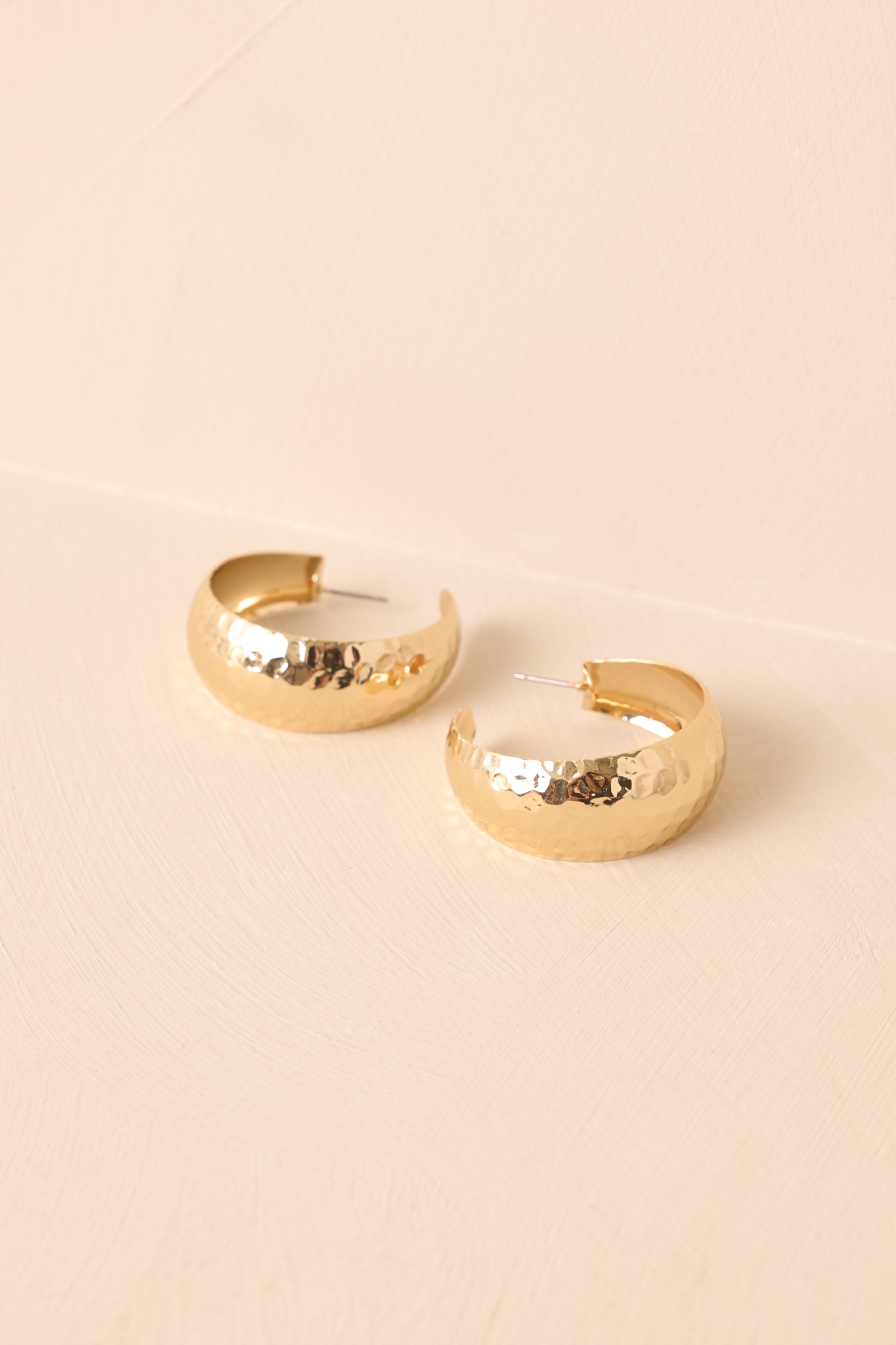 A detailed shot of the hammered gold open hoop earrings highlighting the textured finish and tapered silhouette.