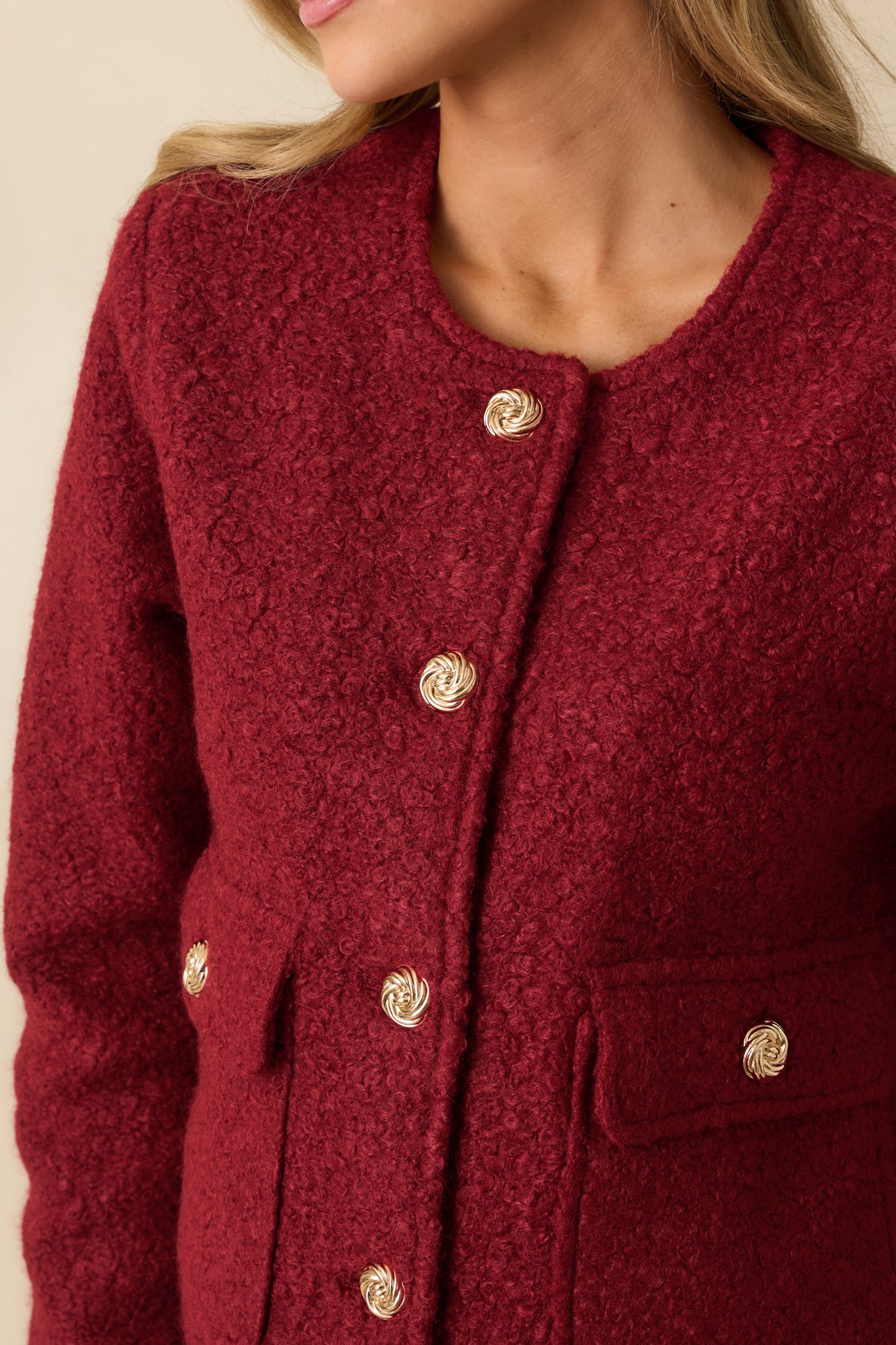 Detailed shot of the cherry red bouclé jacket showcasing the gold button closures, front flap pockets, and textured fabric.