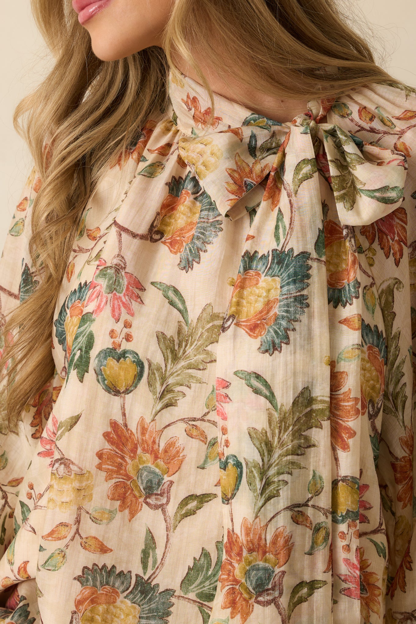Detailed look at the bow tie neckline, balloon sleeve cuff, and delicate floral pattern of the beige blouse.