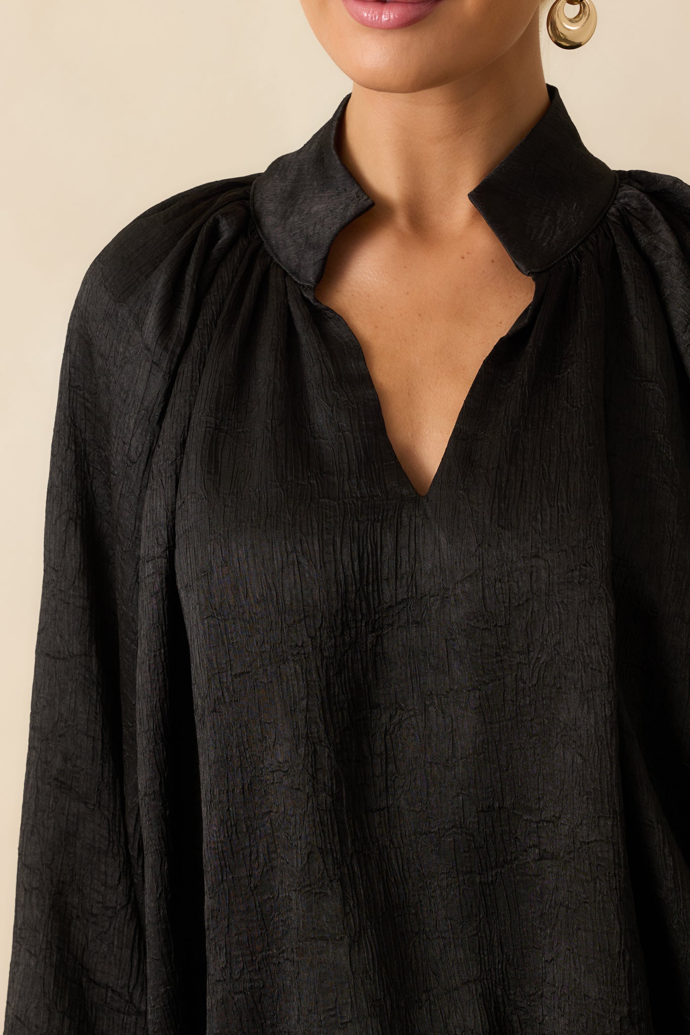 Detailed shot of the black satin top showcasing the ruched neckline, gathered sleeve cuffs, and soft textured fabric.