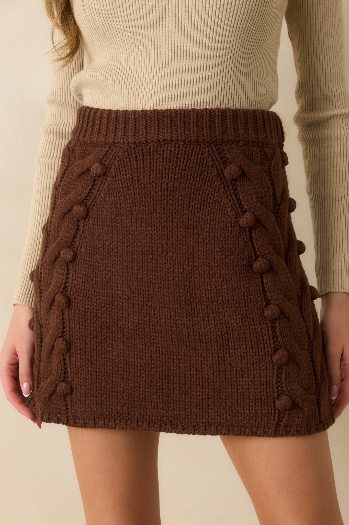 Detailed view of bobble accents and raised cable knit design on the chocolate brown skirt.