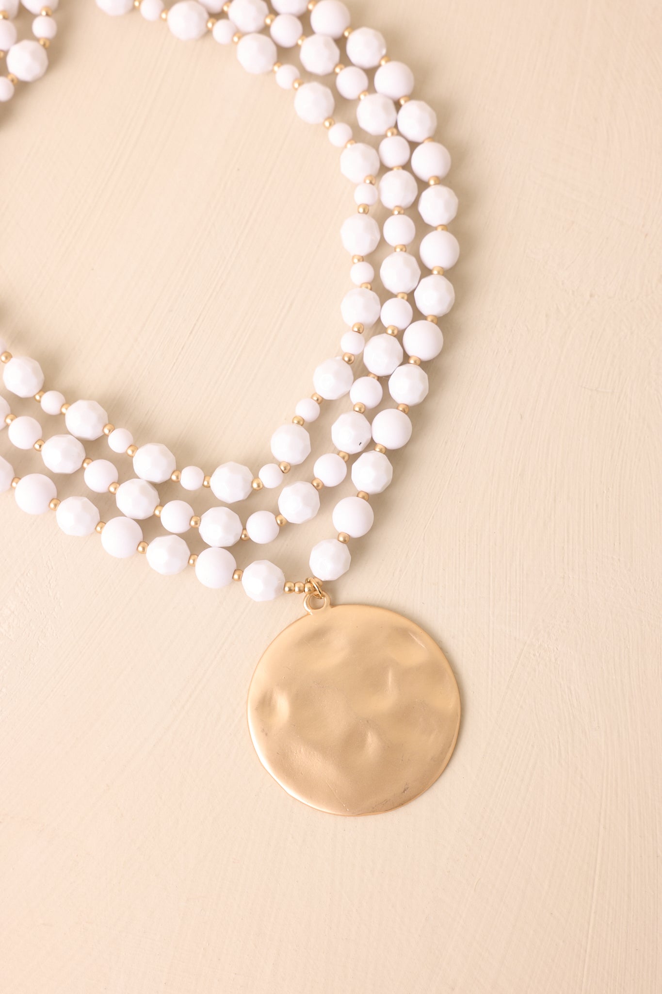 A detailed shot of the layered necklace highlighting its hammered matte gold disc, bead pattern, and gold hardware.