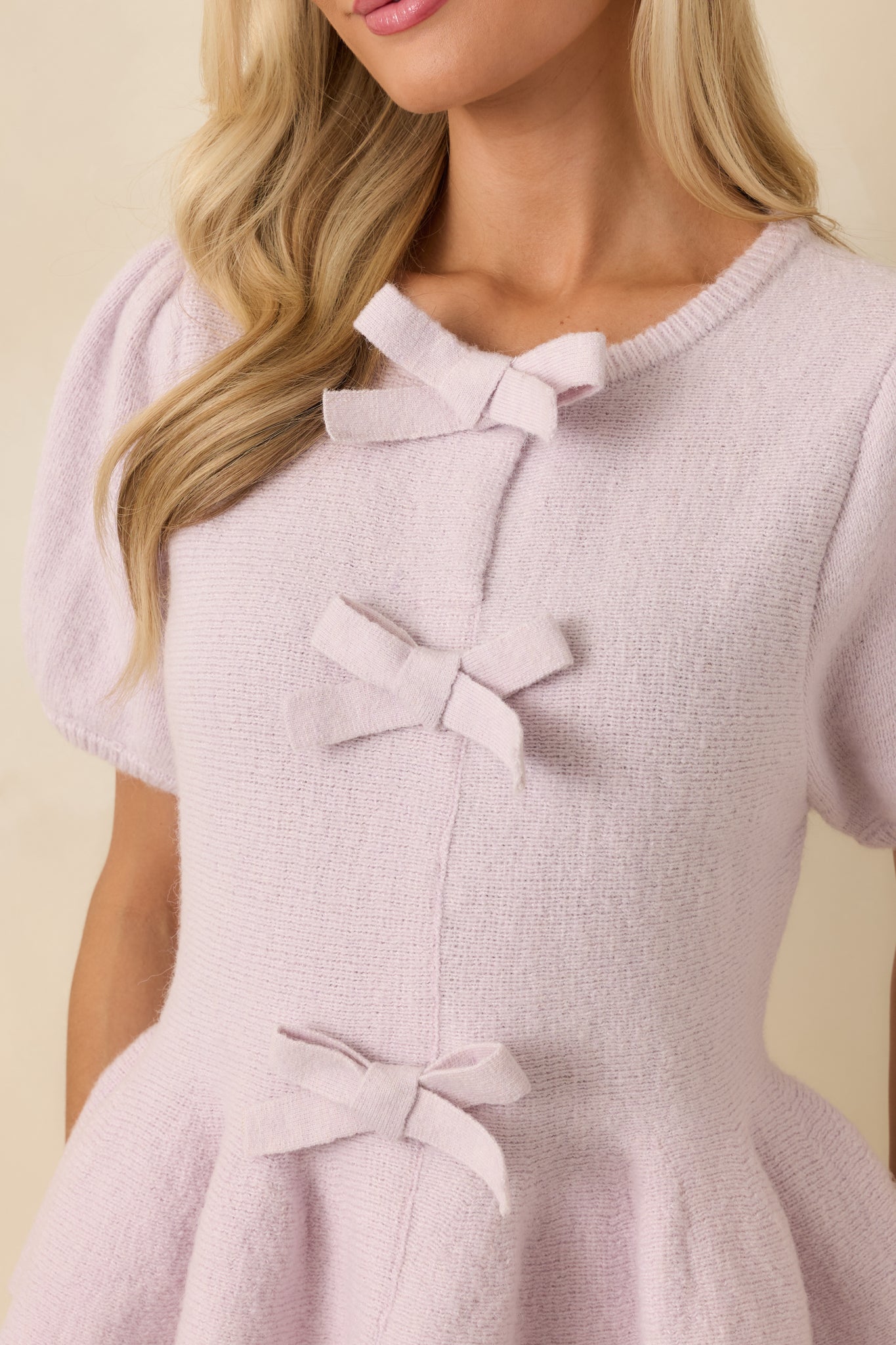 Detailed view of one decorative bow on the front of a lavender knit top, showing knit texture and soft stretch.