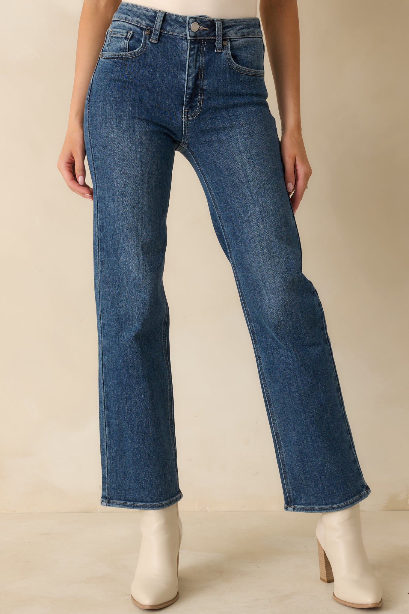 Detailed view of front of medium blue jeans emphasizing waistband, button closure, and smooth denim texture.