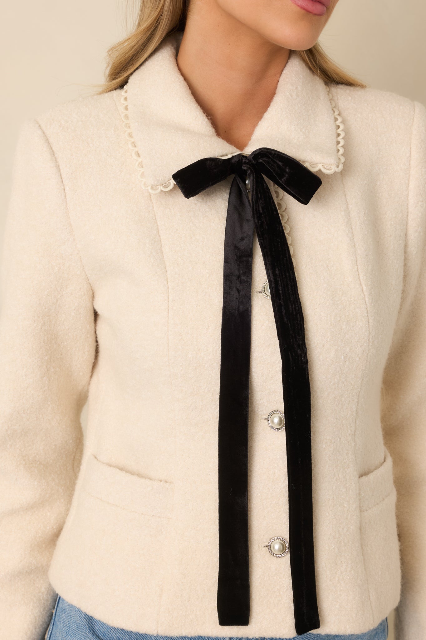 Detailed view of wool fabric, scalloped collar edge, and pearl button closure on natural-colored jacket.