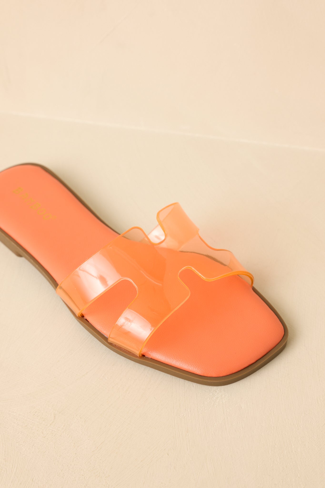 Detailed view of the clear vinyl strap over the orange footbed, highlighting texture contrast and sleek surface finish.