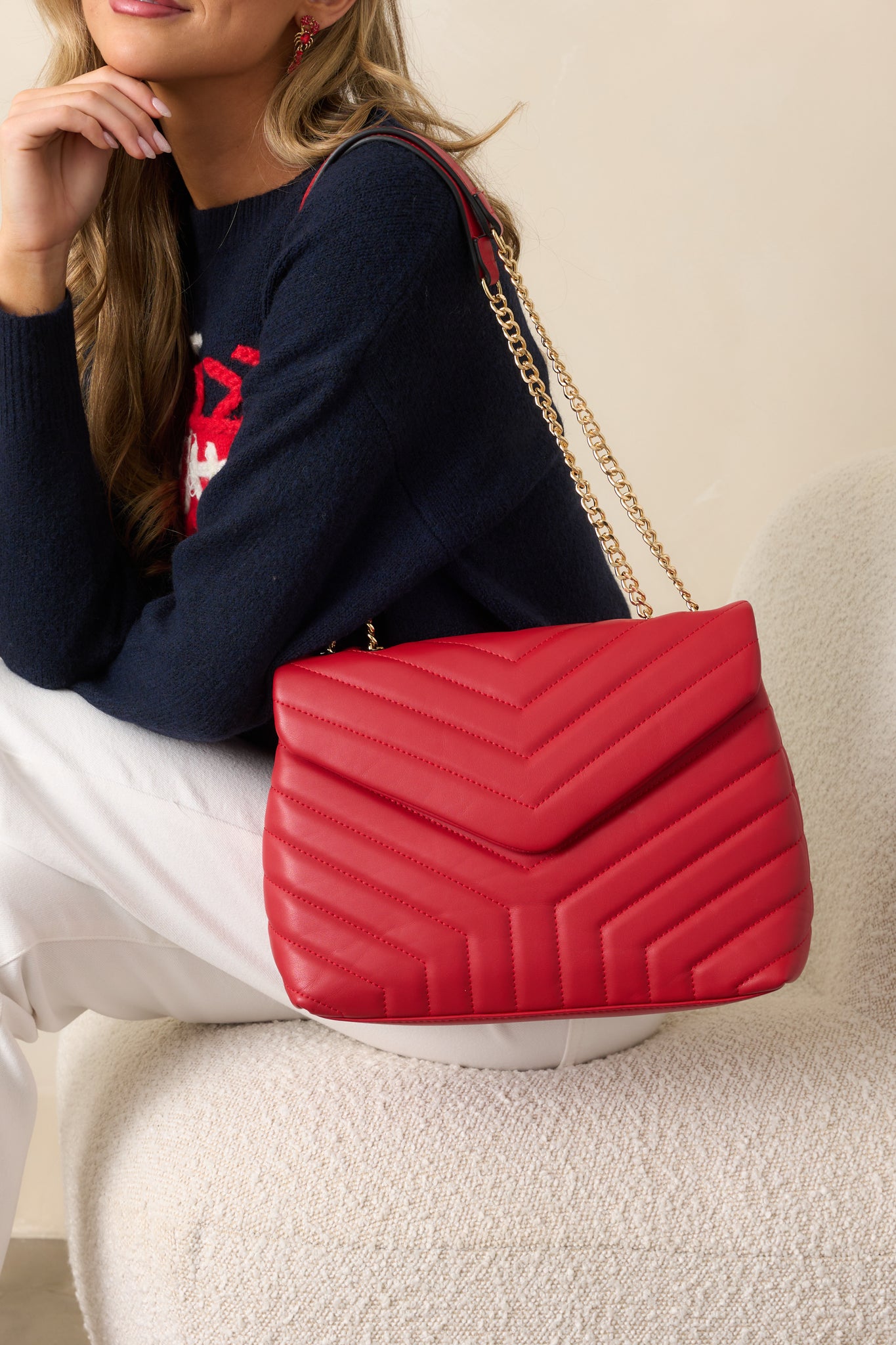 A detailed view of the two gold chain handles with red faux leather handles, highlighting the quilted design of the red handbag and the fold over closure at the top.
