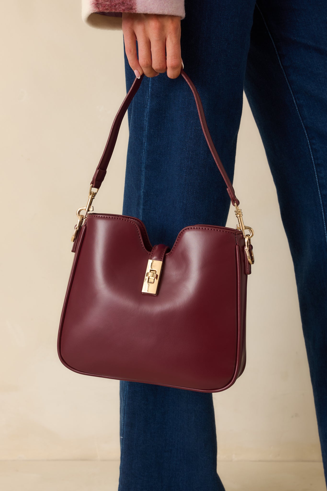 Detailed view of the gold twist-lock hardware and stitching on the wine red faux leather handbag.