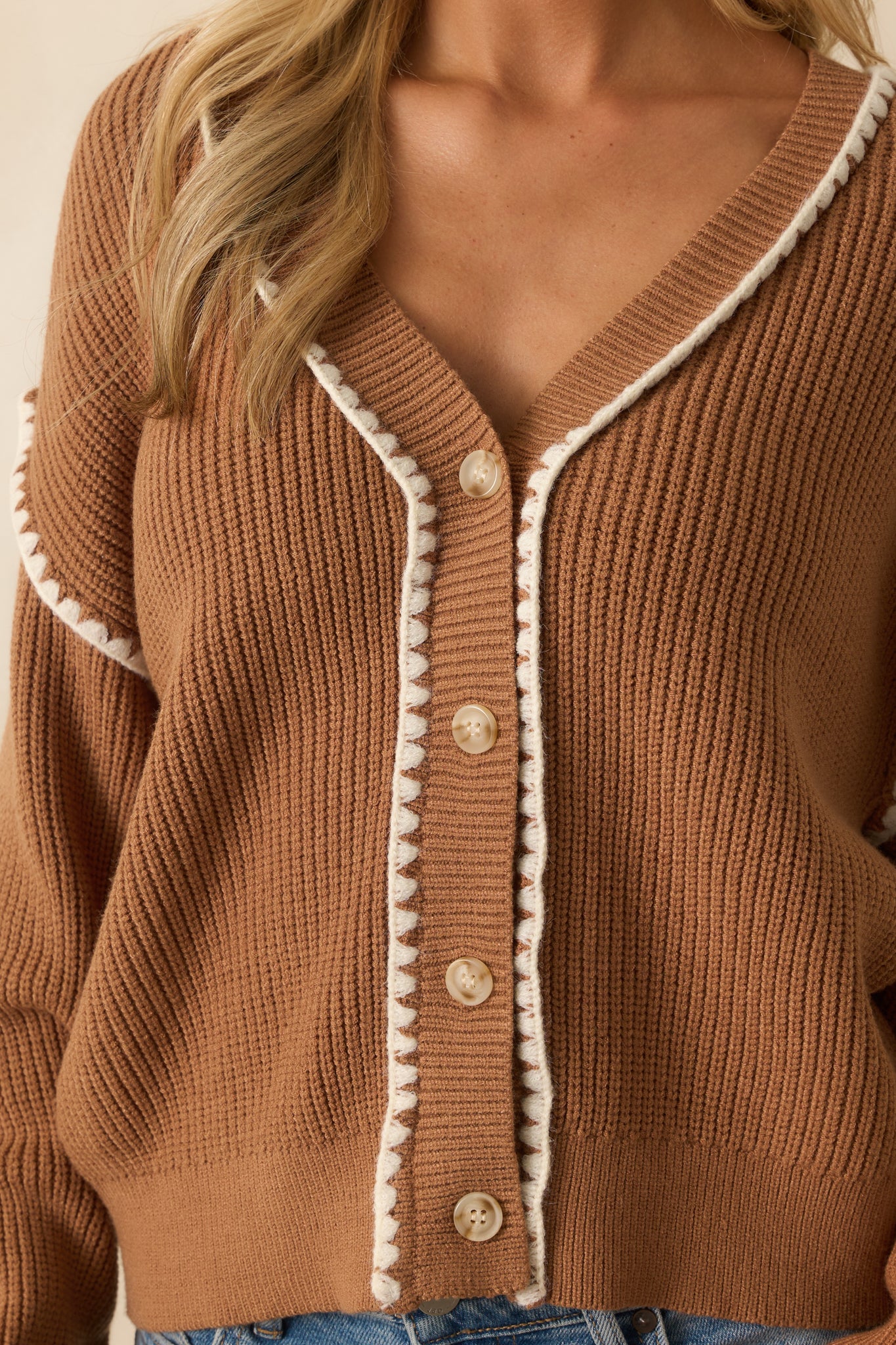 Detailed view of the white whipstitch trim along the edges and sleeves of the camel brown cardigan.