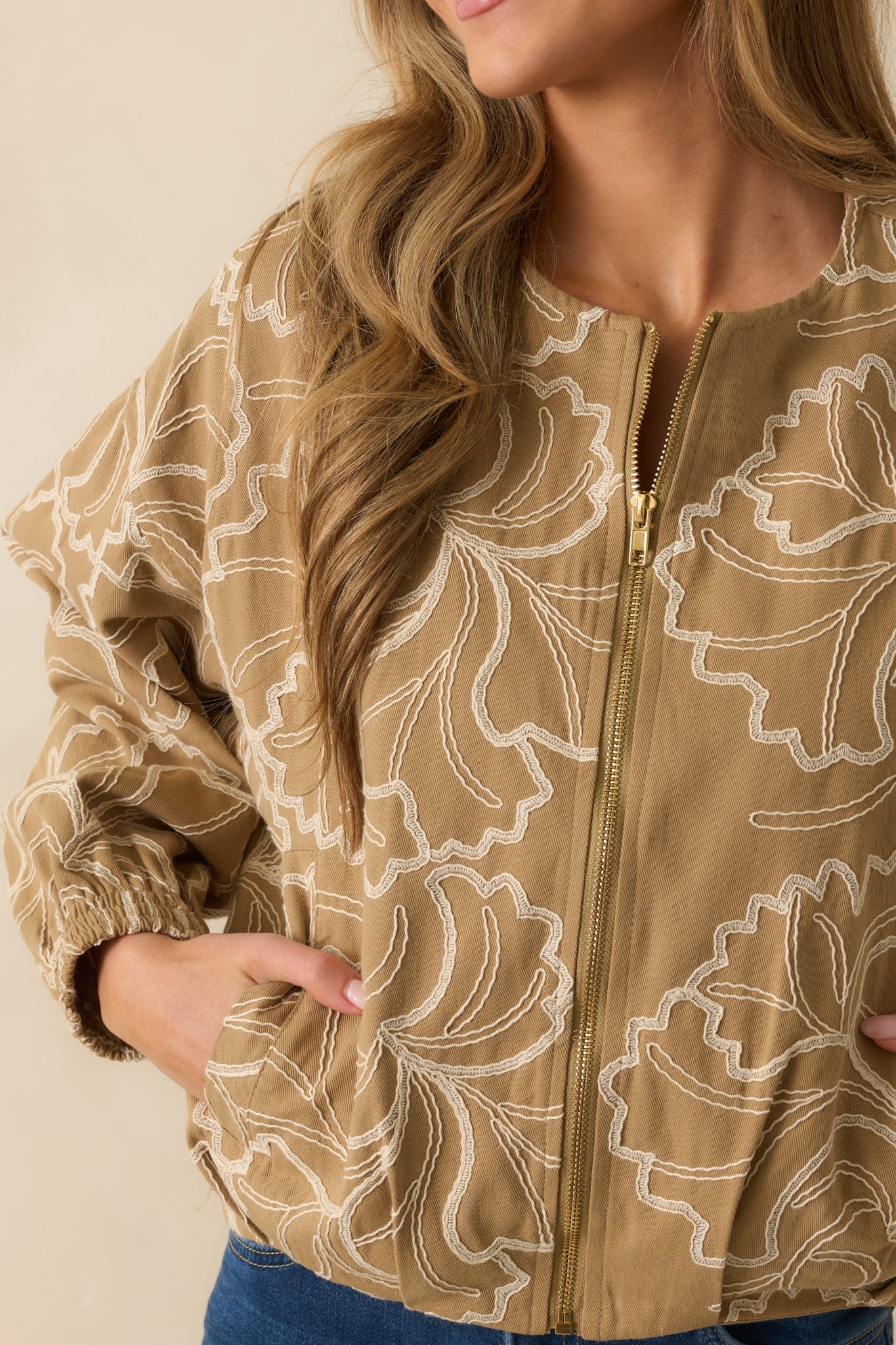 Detailed view of the tan cotton fabric with delicate ivory floral embroidery and fine stitching.