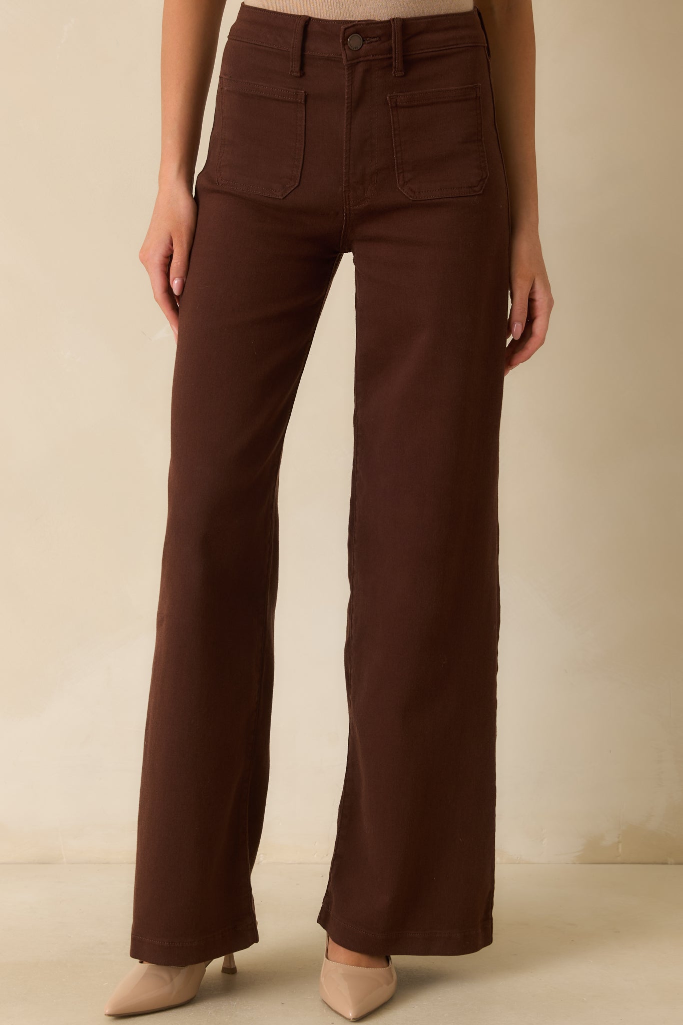 Detailed view of the zipper-and-button closure, belt loops, and front pocket stitching on brown jeans.