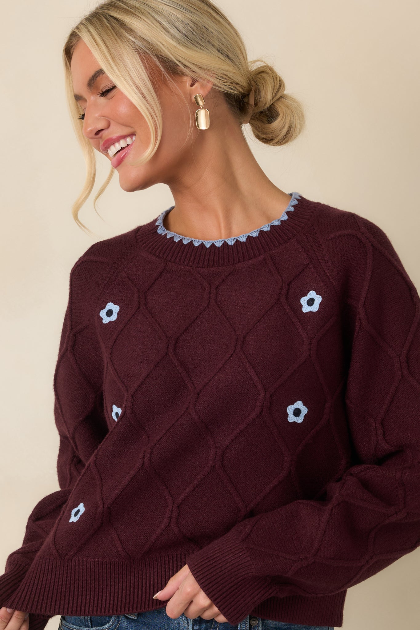 Detailed front view of the sweater showcasing the raised diamond-knit pattern, blue floral embellishments, and soft ribbed trim.