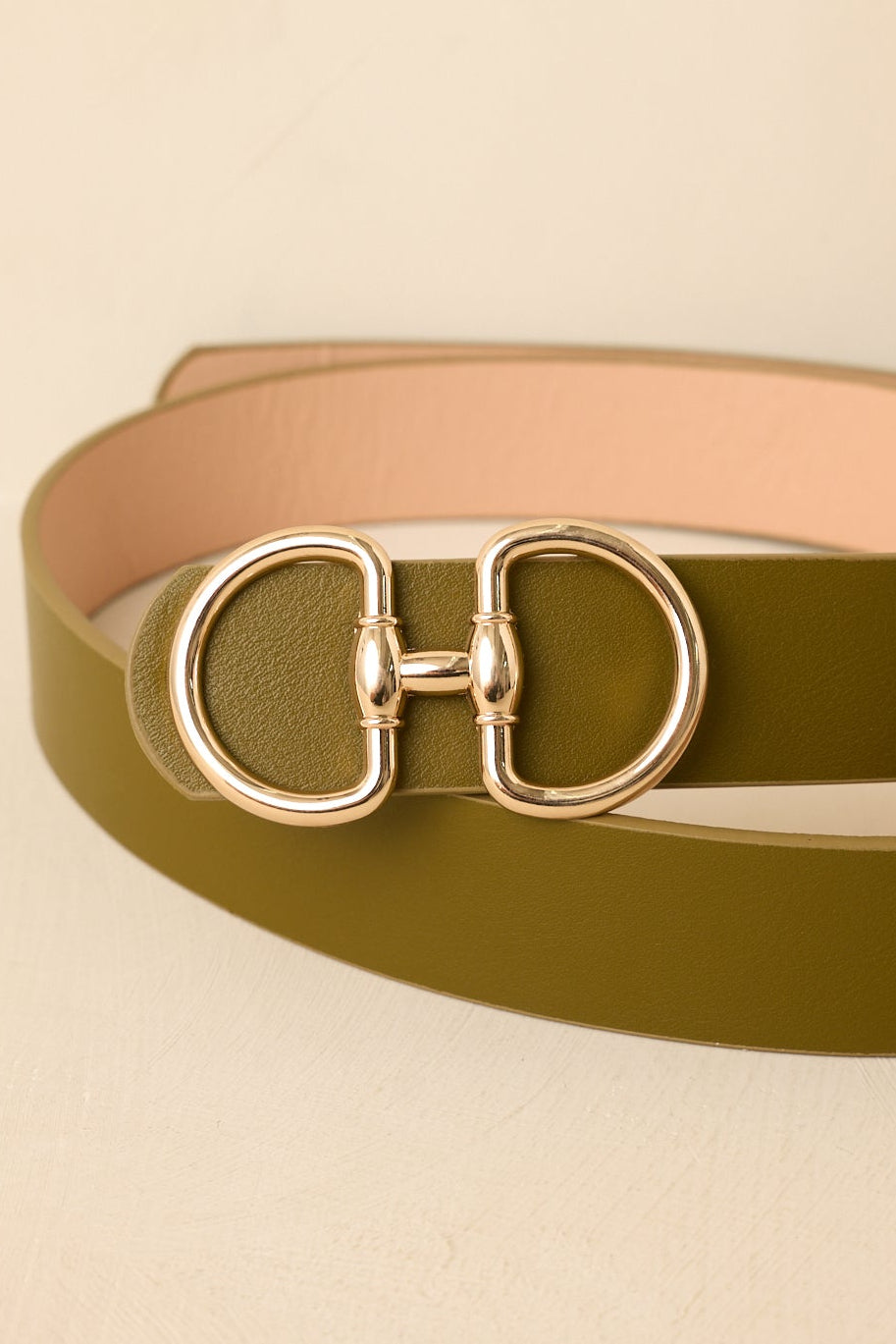 Close-up of the gold-tone double ring buckle and smooth olive faux leather texture.