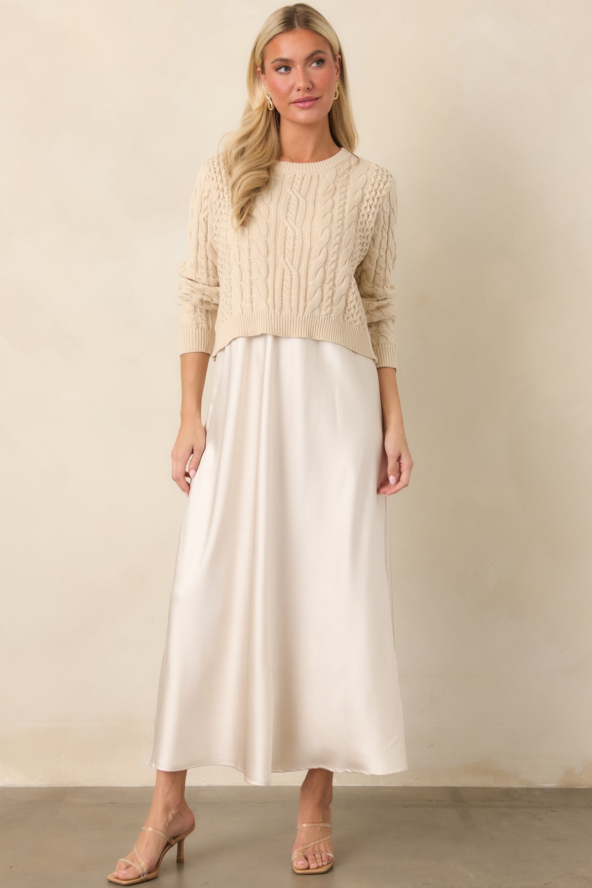 Draped satin maxi dress paired with a cropped cotton sweater featuring intricate textured cable-knit patterns.