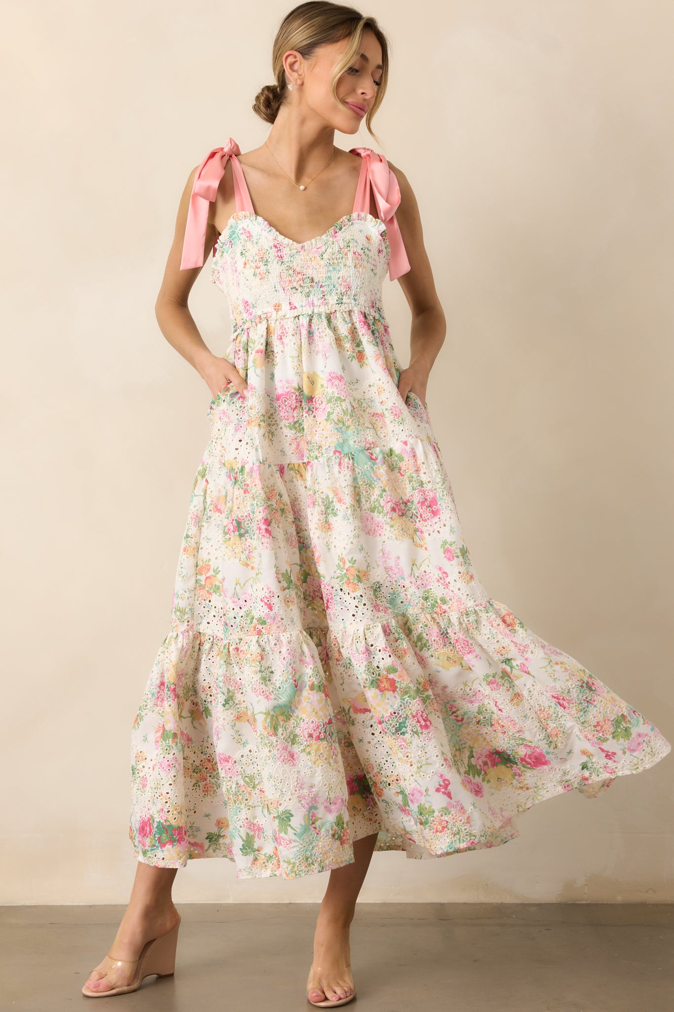 The light pink floral dress features a sweetheart neckline, pink satin self-tie bow straps, embroidered eyelet details, and a tiered skirt, offering both style and functionality with its smocked bust and pockets.