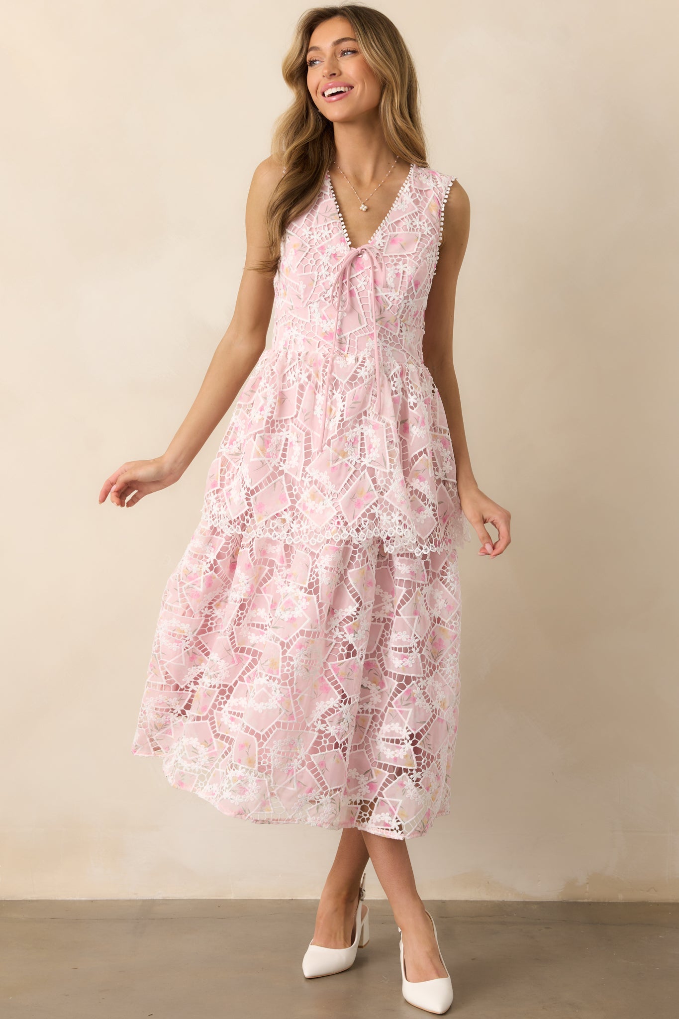 A feminine dress featuring a v-neckline with a pink bow, delicate floral embroidery, and layered tulle panels for added dimension.