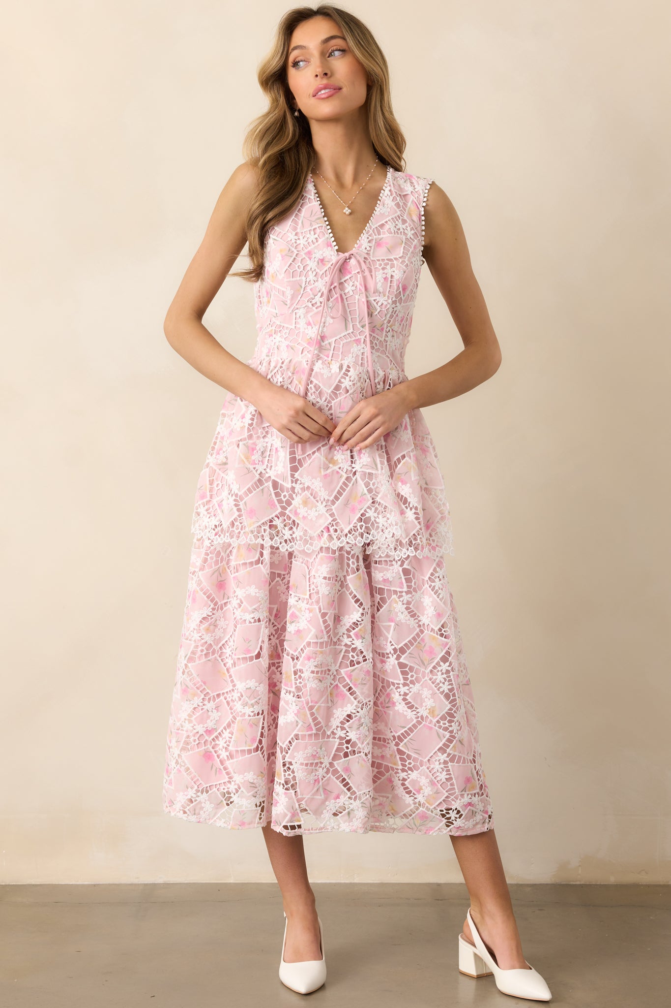 A light and airy dress with intricate white embroidery over a pink base, a v-neckline with a dainty bow, and a tiered silhouette.